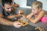 Bei der Kinderphysiotherapie spielt der Therapeut in Mönchengladbach mit einem kleinem Mädchen ein Holzspiel zeug mit Perlen